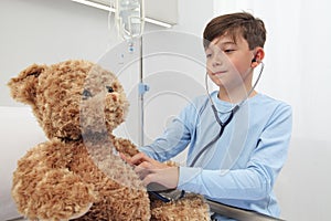 Child in hospital room playing with a stethoscope and a teddy bear imitating doctor photo