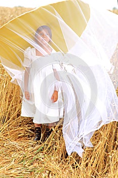 Child in a huge yellow hat in a wheat field in summer