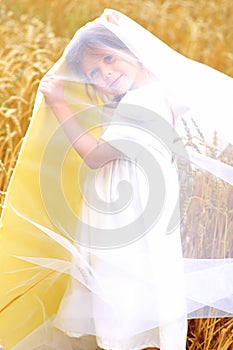 Child in a huge yellow hat in a wheat field in summer
