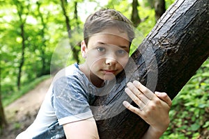 Child hugging tree trunk in forest