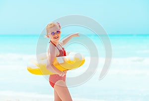 Child with inflatable lifebuoy pointing at something on beach