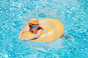 Child with inflatable ring in swimming pool. Kid boy swim in outdoor pool of tropical resort. Hot Summer. Water toys and