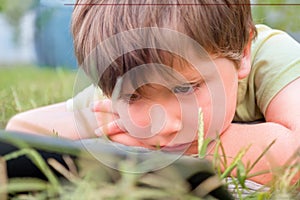 Child with ipad on green grass. Portrait of boy with tablet. Eye problems caused by using tablets too much. Health care