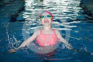 Child is jumping and having fun in swimming pool. Girl in goggles and swimming cap