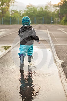 Child jumping in puddle in waterproof coat and rubber boots