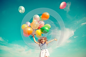 Child jumping with toy balloons in spring field