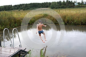 Child jumping from wooden bridge into pond