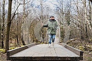 Child jumping on a wooden trampoline in the woods engages in a funny outdoor activity. Lighthearted kid hopping on a board