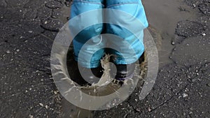 A child jumps on a muddy puddle in winter in rubber boots and pants.Stains and dirt on children`s clothes after a walk.Warm winter