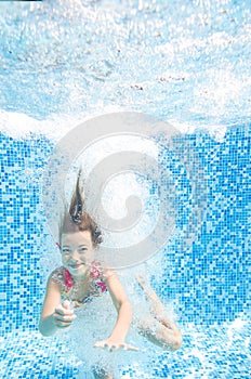 Child jumps to swimming pool and swims underwater, little active girl dives and has fun under water, healthy kids sport