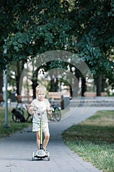 Child on kick scooter in park. A boy is riding on the kick scooter in a park. The concept of a healthy lifestyle. Kids sport