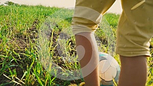 A child kicks a soccer ball with his feet on the high green grass in the field, rear view on his feet