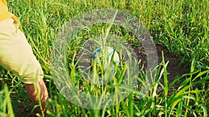 A child kicks a soccer ball with his feet on the high green grass in the field, view of the legs from the side