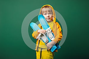 Child kid boy in yellow sweatshirt with skis in his hands. Children leisure and sports concept, in green background