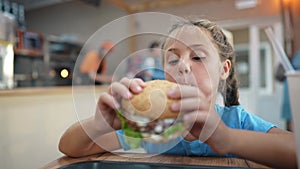 child kid eating a burger in a cafe. fast food nutrition health concept. daughter girl eats with pleasure hamburger. a