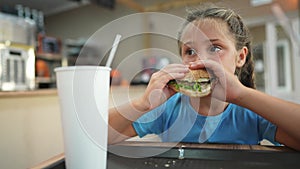 child kid eating a burger in a cafe. fast food nutrition health concept. daughter girl eats with pleasure hamburger. a