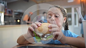 Child kid eating a burger in a cafe. Fast food nutrition health concept. Daughter girl eats with pleasure hamburger. A