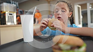 child kid eating a burger in a cafe. fast food nutrition health concept. daughter girl eats with tasty pleasure