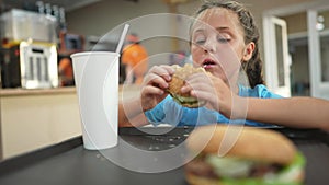 Child kid eating a burger in a cafÃ©. Fast food nutrition tasty health concept. Daughter girl eats with pleasure