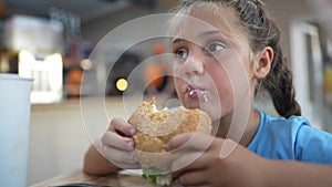 Child kid eating a lifestyle burger in a cafÃ©. Fast food nutrition health concept. Daughter girl eats with pleasure