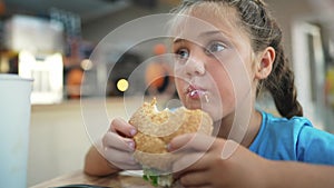 Child kid eating lifestyle a burger in a cafÃ©. Fast food nutrition health concept. Daughter girl eats with pleasure