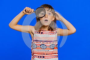 Child kid girl holding magnifying glass, looking into camera with big zoomed funny eye, analysing