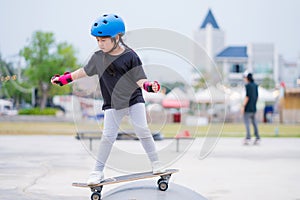 Child or kid girl playing surfskate or skateboard in skating rink or sports park at parking to wearing safety helmet elbow pads