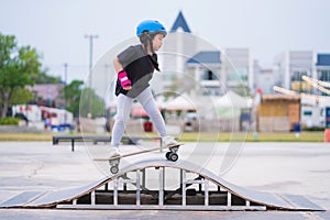 Child or kid girl playing surfskate or skateboard in skating rink or sports park at parking to wearing safety helmet elbow pads