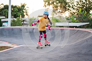Child or kid girl playing surfskate or skateboard in skating rink or sports park at parking to wearing safety helmet elbow pads