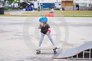 Child or kid girl playing surfskate or skateboard in skating rink or sports park at parking to wearing safety helmet elbow pads