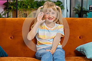 Child kid girl smiling friendly at camera, waving hands gesturing hello hi greeting at home on couch