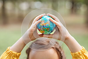 Child kid girl in a yellow raincoat holding globe in a hands outdoor in park or forest. World Earth Day concept. Green Energy,