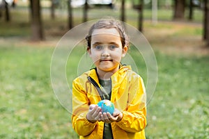 Child kid girl in a yellow raincoat holding globe in a hands outdoor in park or forest. World Earth Day concept. Green Energy,