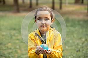 Child kid girl in a yellow raincoat holding globe in a hands outdoor in park or forest. World Earth Day concept. Green Energy,