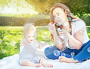 Child (kid) having fun with mother and soap bubbles in a sunny summer day. Caucasians happy baby (boy).