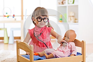 Child in kindergarten. Kid in nursery school. Little girl preschooler playing doctor with doll.