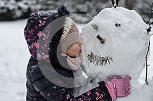 Child kissing a cold snowman in winter time
