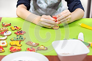 Child in the kitchen. Decorating cookies with colorful icing. The child`s hands squeeze the frosting in yellow.