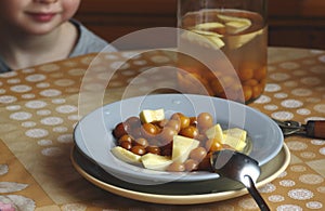 Child at the kitchen  table with stewed fruit compote- zucchini and cherry plum on the plate