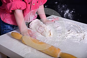 The child knead the flour, the dough with a rolling pin rolls.