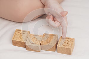 The child laid out the word toys made of wooden cubes, close-up. A small child learns the English alphabet, learns to