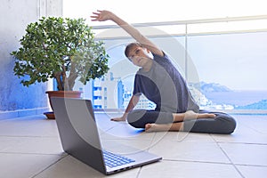 Child with laptop doing sport exercises, practicing yoga on balcony. Sport, healhty lifestyle, active leisure. Stay at