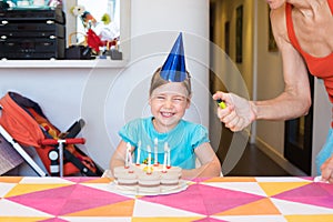 Child laughing and woman hand lighting candles on birthday cake