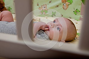 The child lays in a crib and sits a finger. Happy baby recently slept in his crib