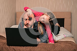 A child lays a toy spider on a manÃ¢â¬â¢s head. Daughter prevents dad from working on a computer. Little girl scares father with an