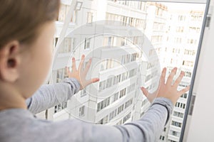 The child leaned on the mosquito net of an open window in an apartment on a high floor, danger, children alone at home