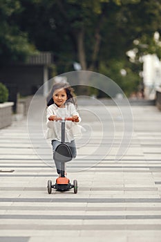 Child learn to ride scooter in a park on sunny summer day