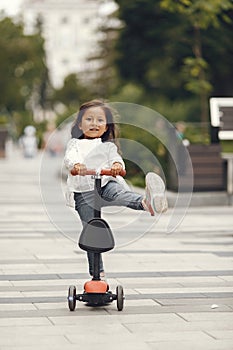 Child learn to ride scooter in a park on sunny summer day