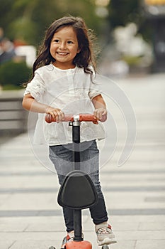 Child learn to ride scooter in a park on sunny summer day