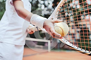 Child learning to play tennis in the sport club. Cropped image of a girl child preparing to serve tennis ball. Little girl tennis